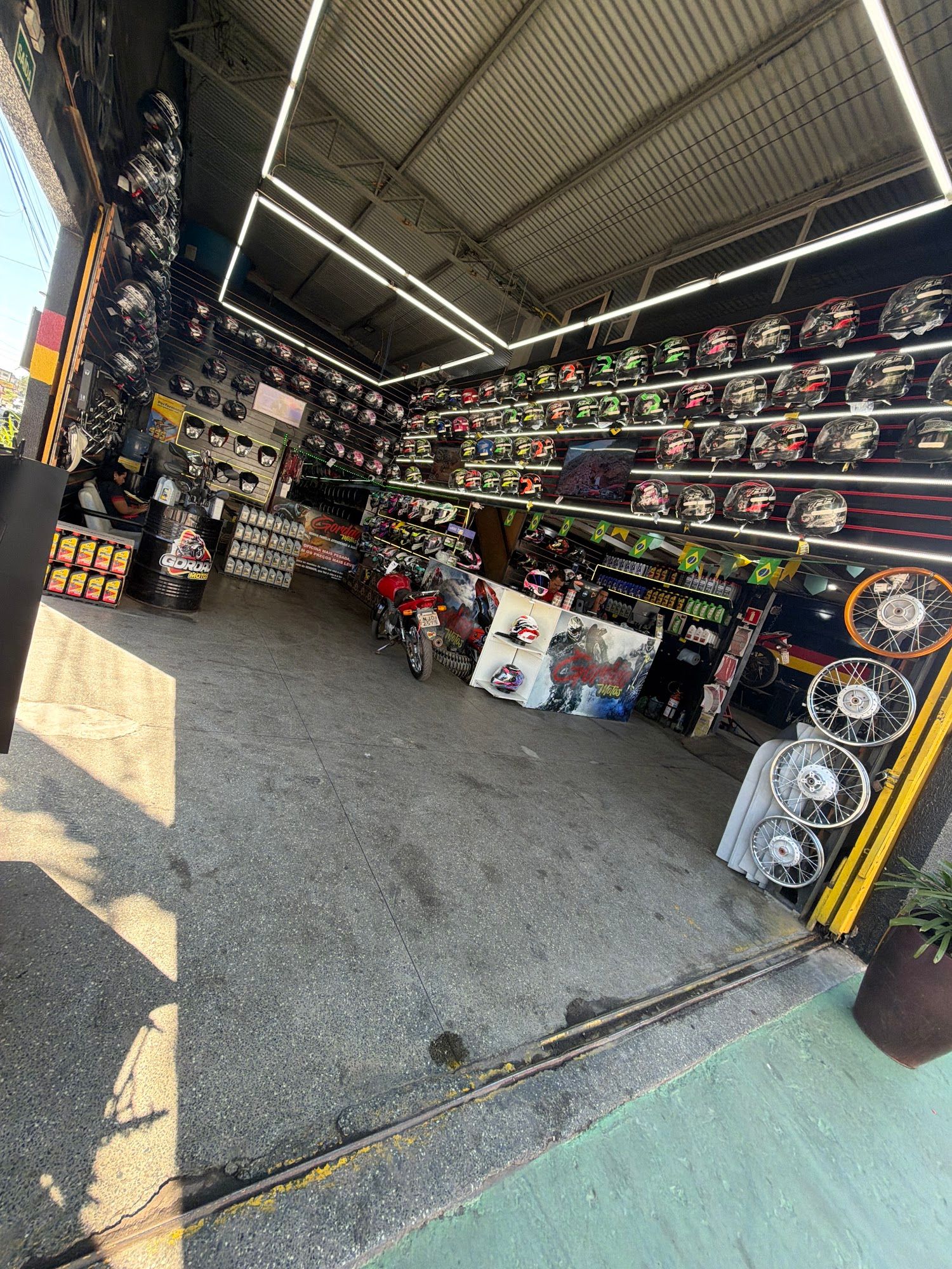 Fachada da Gordão Motos com a porta aberta, salão com paredes de capacetes iluminadas e rodas de moto expostas